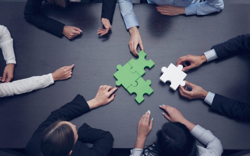 A group of people sitting around a table with puzzle pieces.