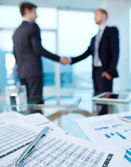 Two men shaking hands in front of a table.